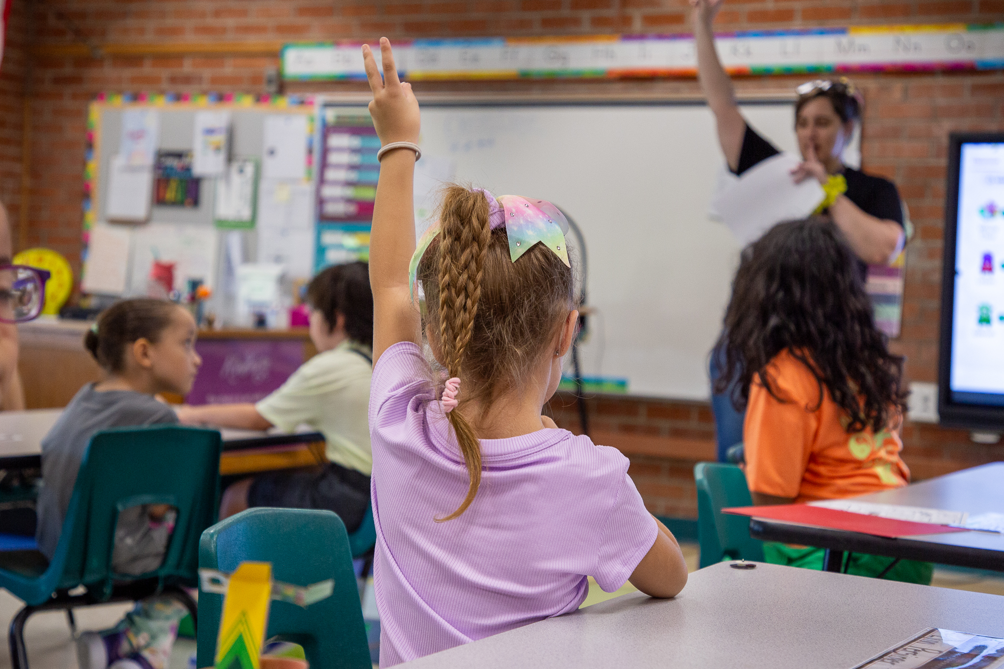 A little girl raises her hand in class