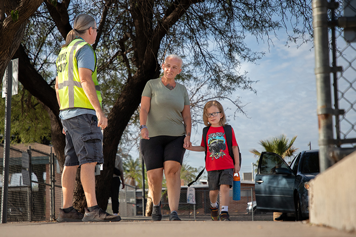 A woman in a yellow safety vest welcomes families onto school grounds