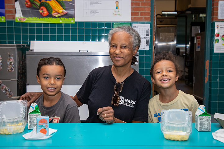 A woman sits with two young kids as they enjoy breakfast in the cafeteria