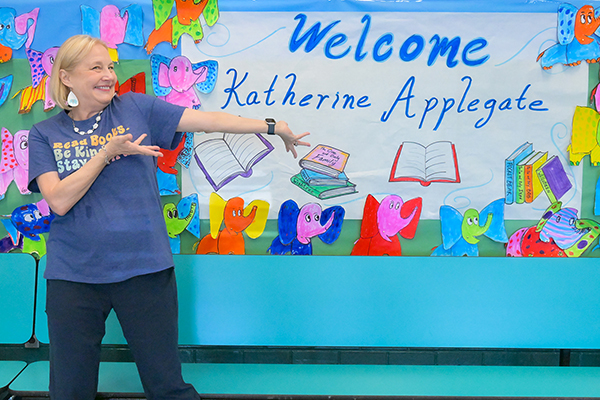 A woman smiles as she points to a banner reading Welcome Katherine Applegate