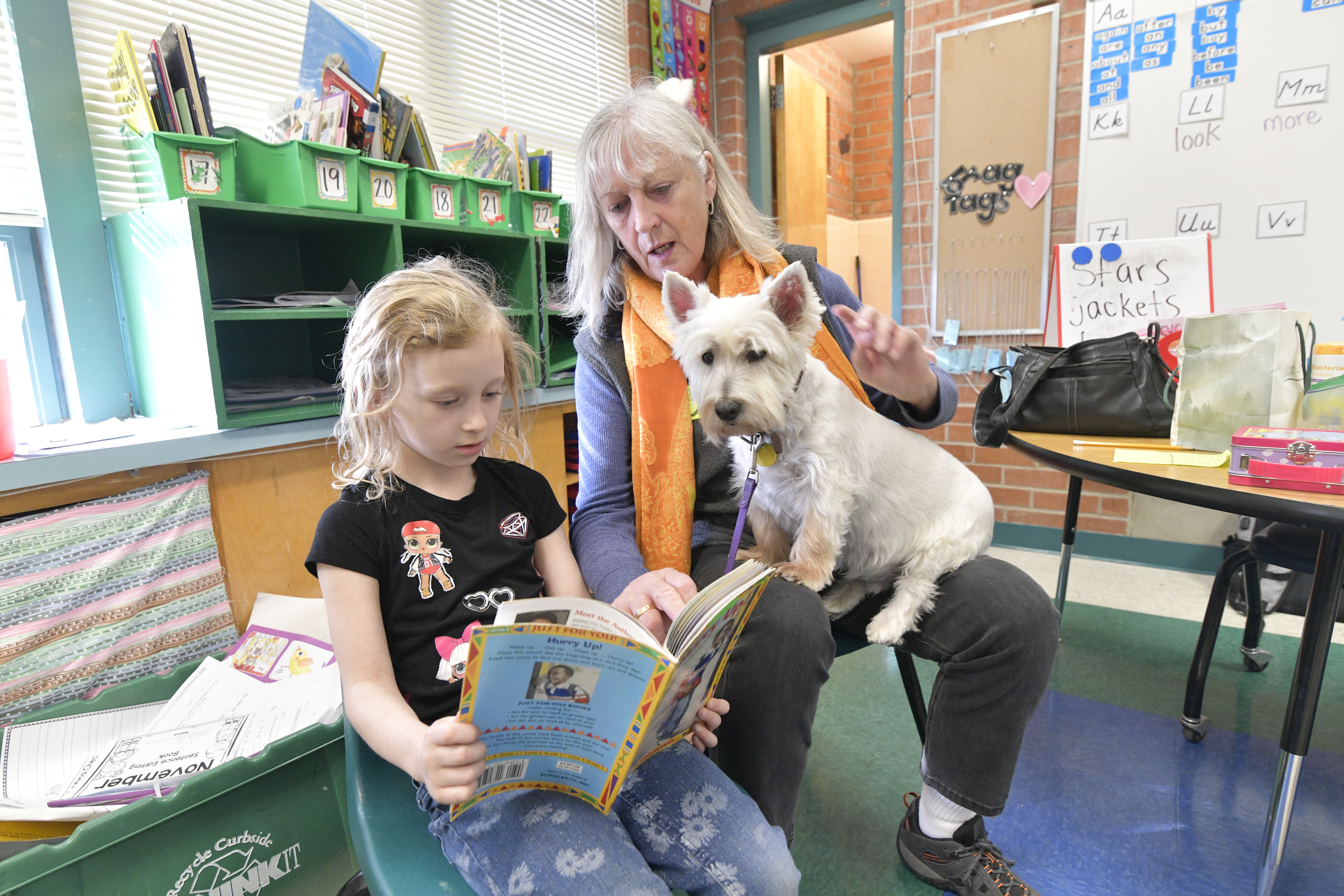 A little girl reads a book to her teacher and a dog